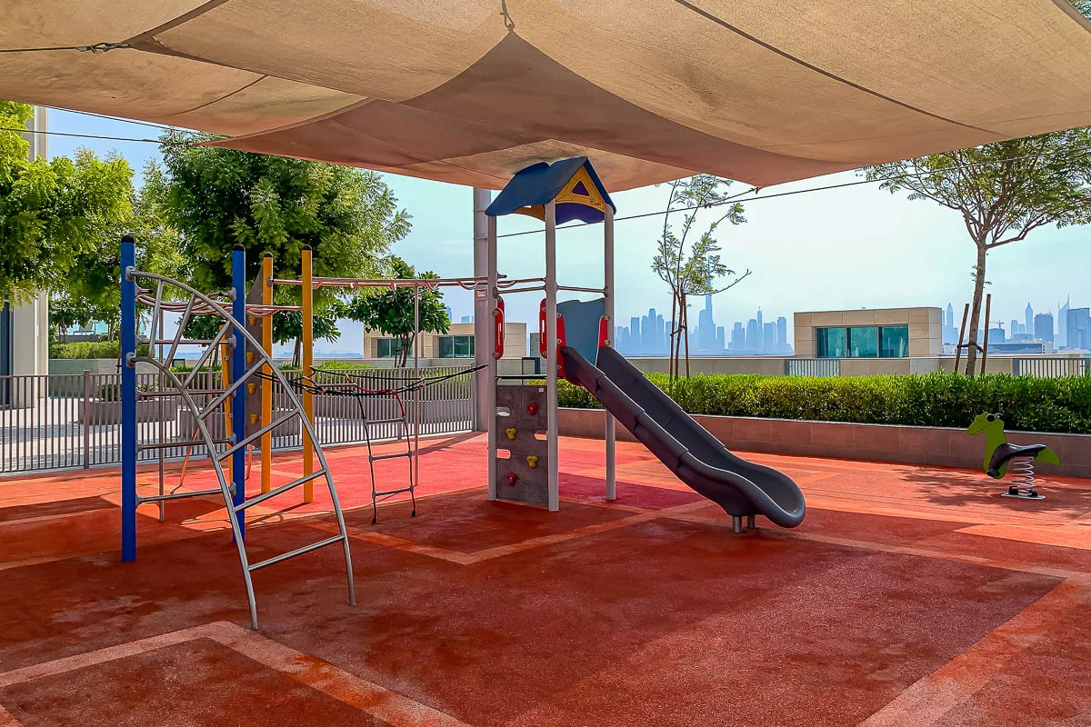 Un parque infantil sombreado con juegos para trepar y un tobogán tiene vistas al horizonte de la ciudad.