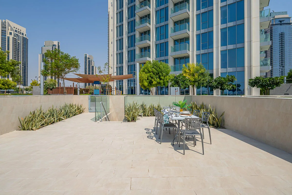 Una terraza al aire libre tiene una mesa de comedor y asientos junto a un edificio acristalado.