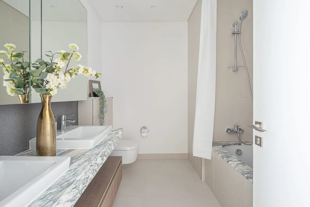 Un baño luminoso con un tocador largo, dos lavabos y una ducha.