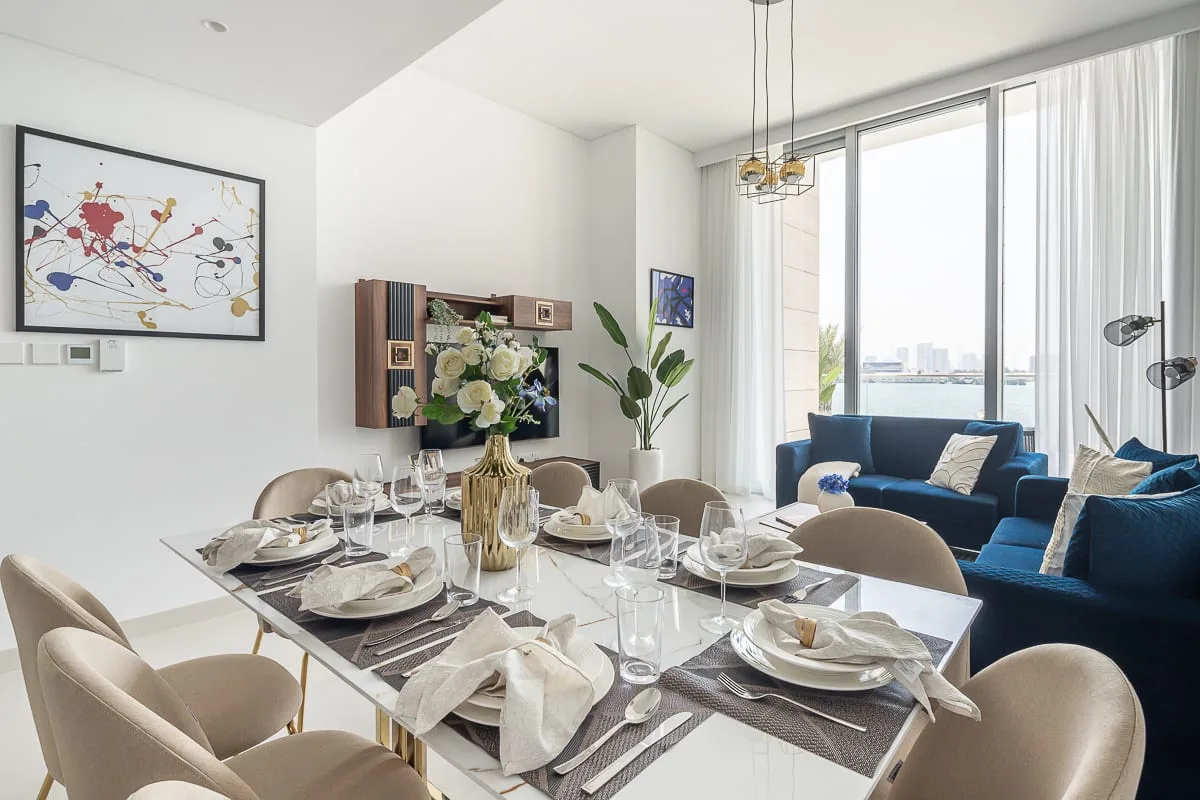 Comedor con la mesa puesta junto a una sala de estar luminosa.