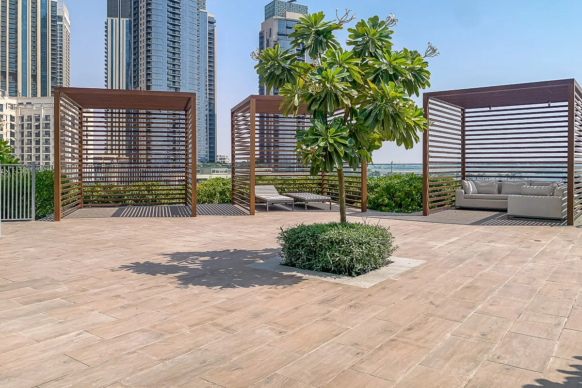 Una terraza pavimentada al aire libre tiene un árbol frondoso y zonas de estar con sombra.
