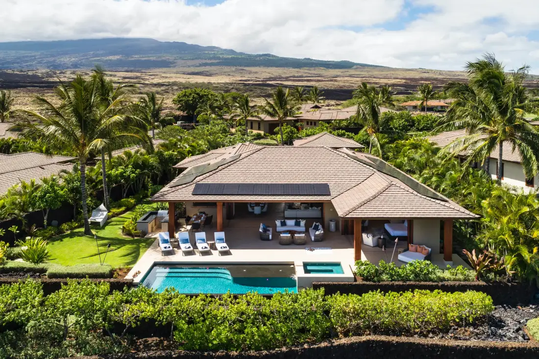 A tropical resort villa with a tiled roof overlooks a pool and landscaped grounds.