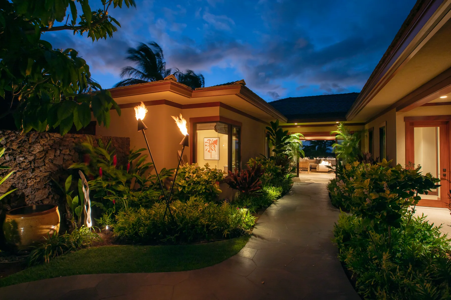 A landscaped walkway runs between warmly lit buildings at dusk.