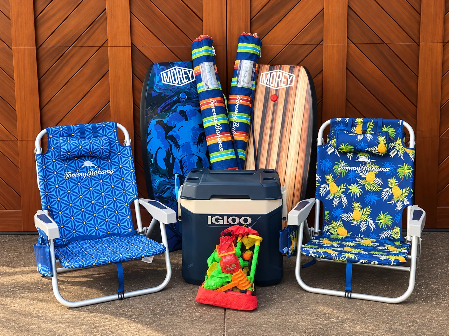 Beach chairs, colorful boards, and a cooler sit against a wooden wall.