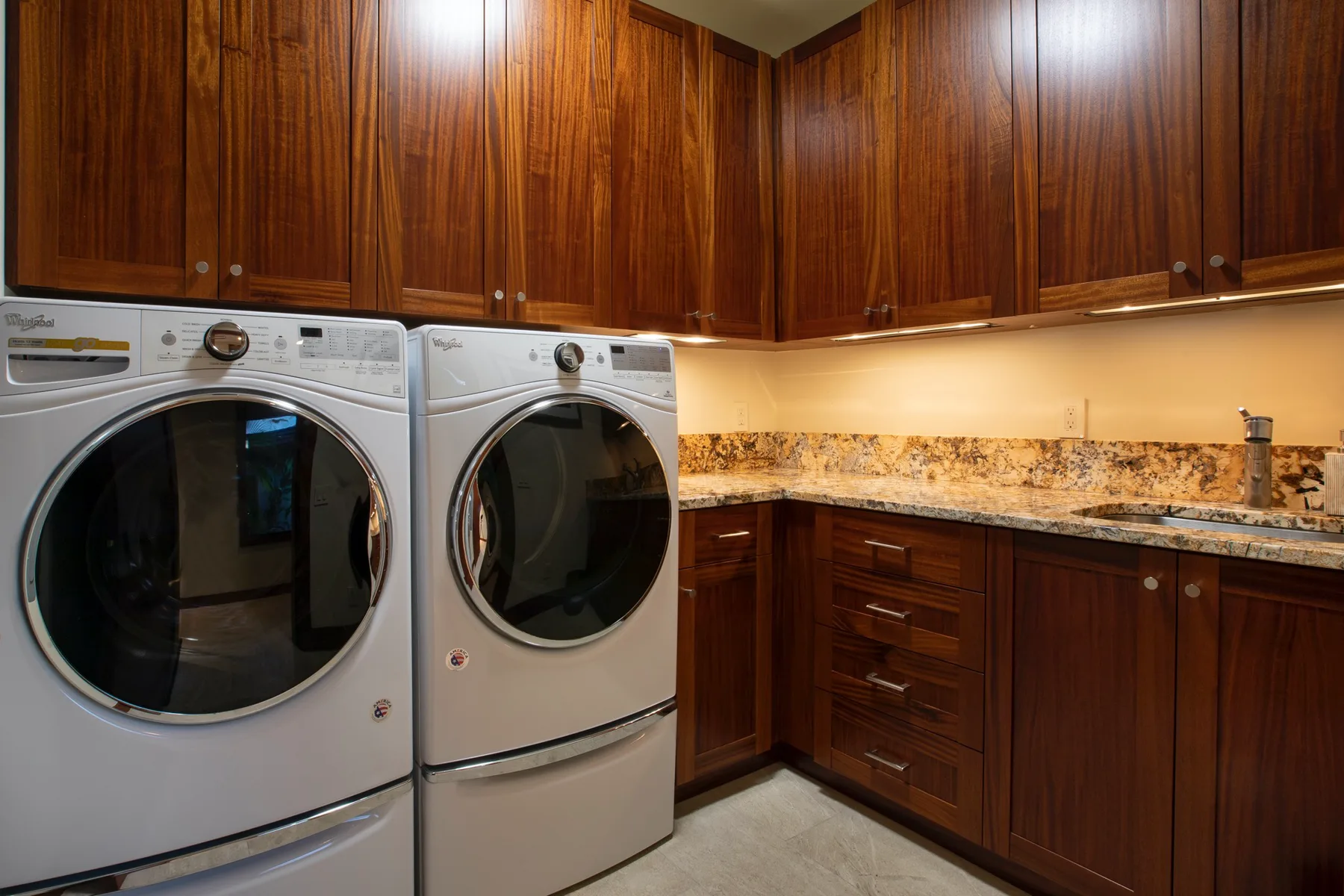A laundry room with a washer and dryer beneath wooden cabinets.