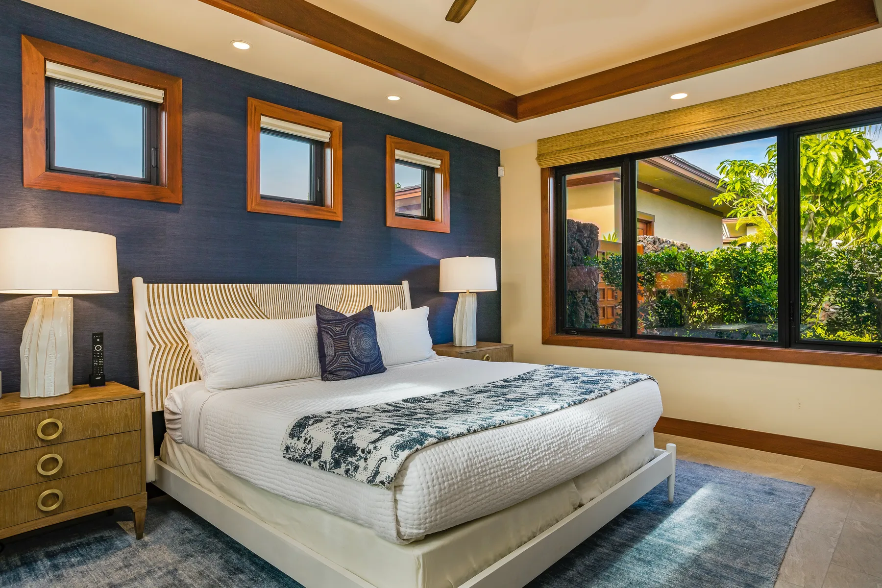 A bedroom with a large bed and windows overlooking greenery.
