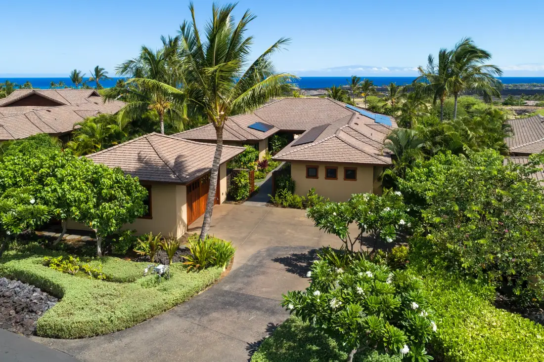 A tropical residential complex with tiled roofs, palm trees, and ocean visible in the distance.