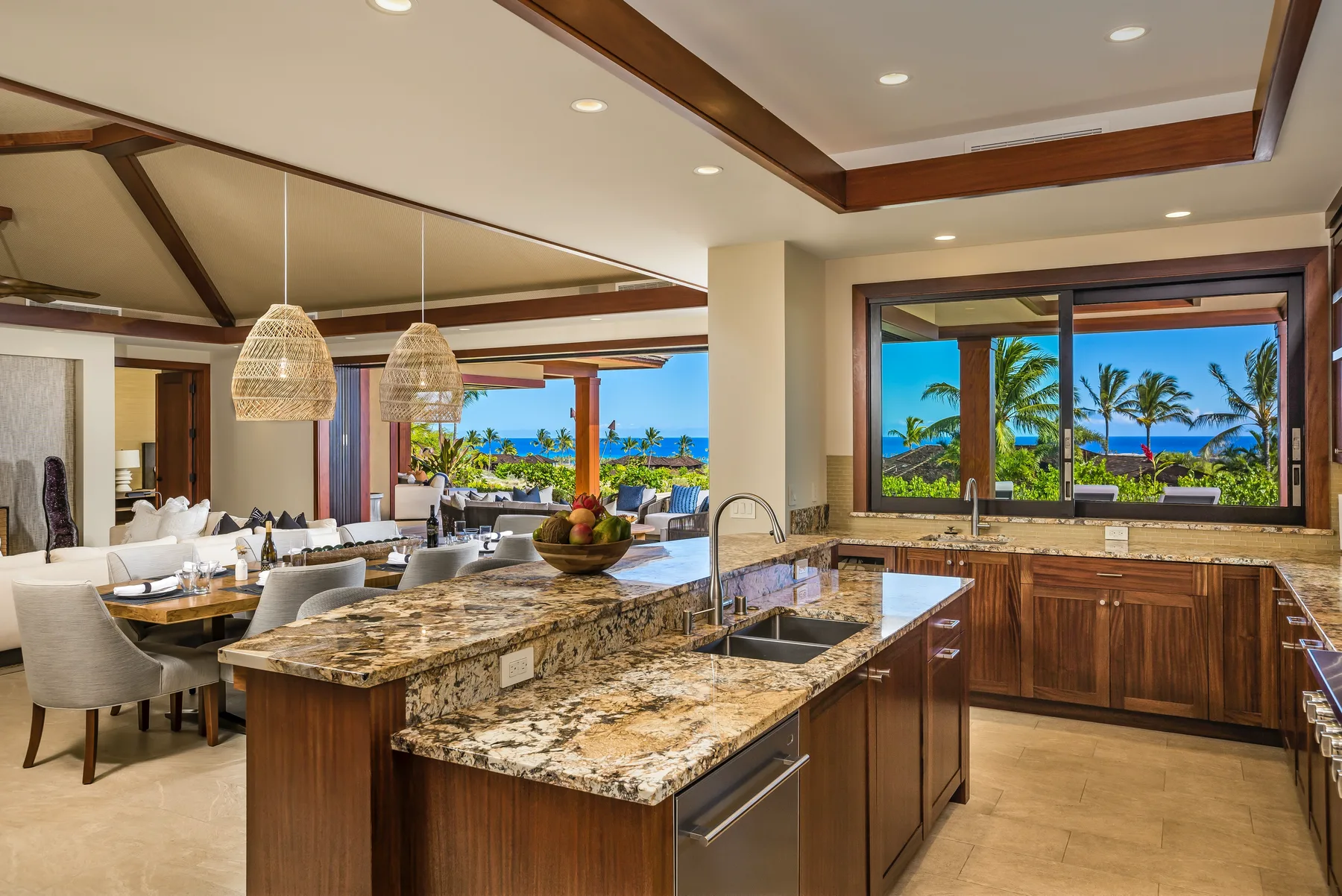 An open kitchen and dining area overlook palm trees and the ocean.