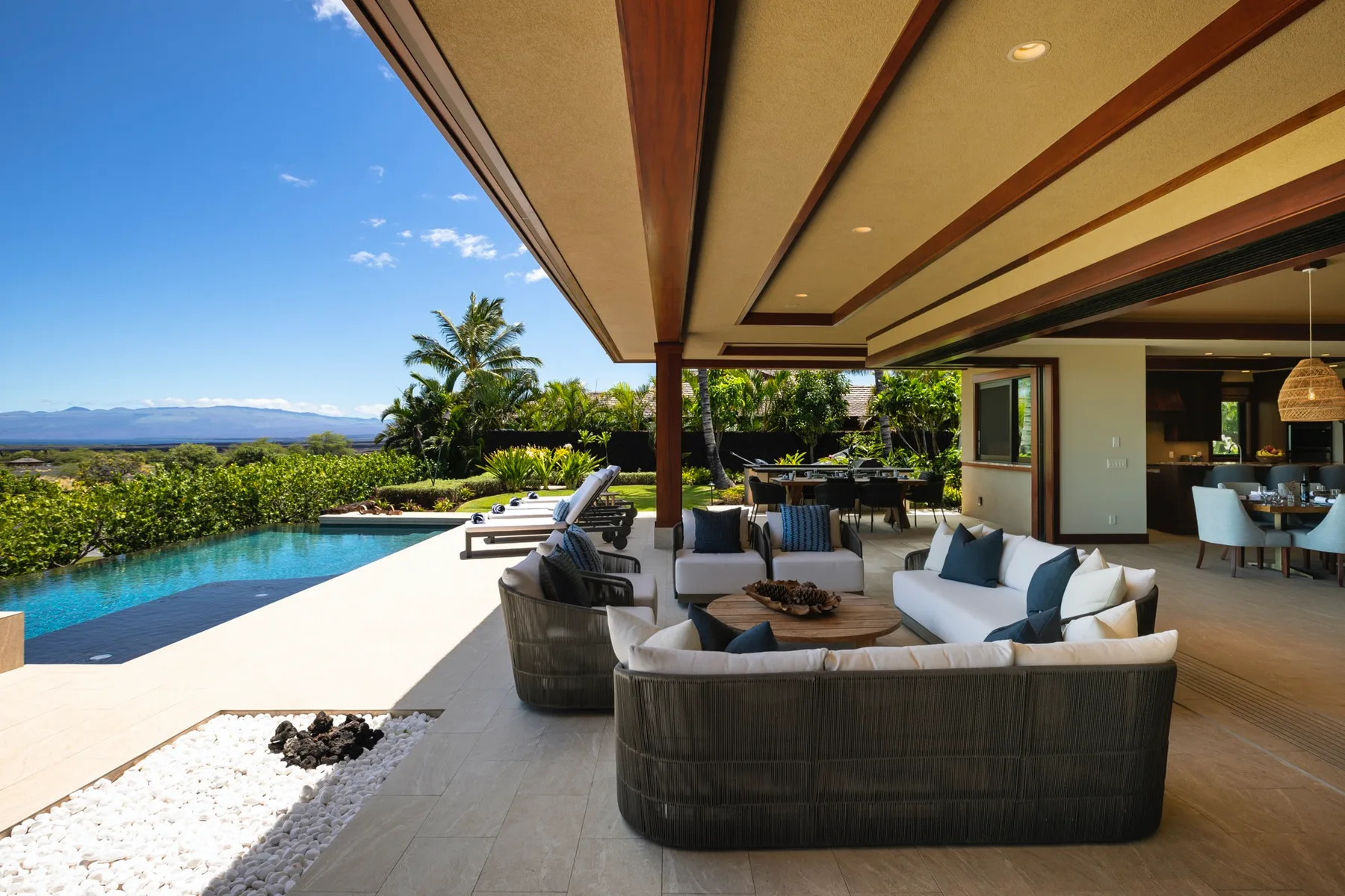 An outdoor patio with lounge seating overlooks a swimming pool and landscaped garden.