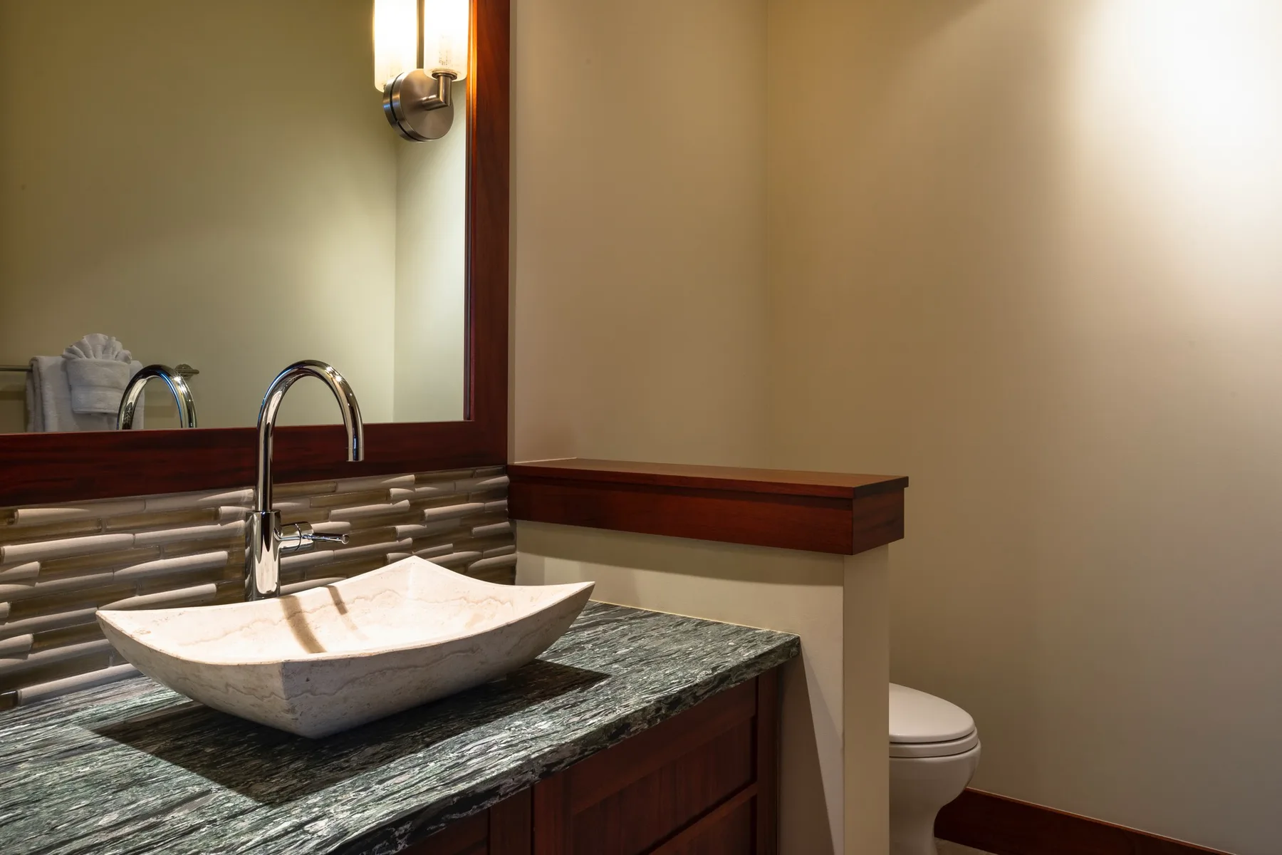 A bathroom vanity with a vessel sink, wall mirror, and toilet.