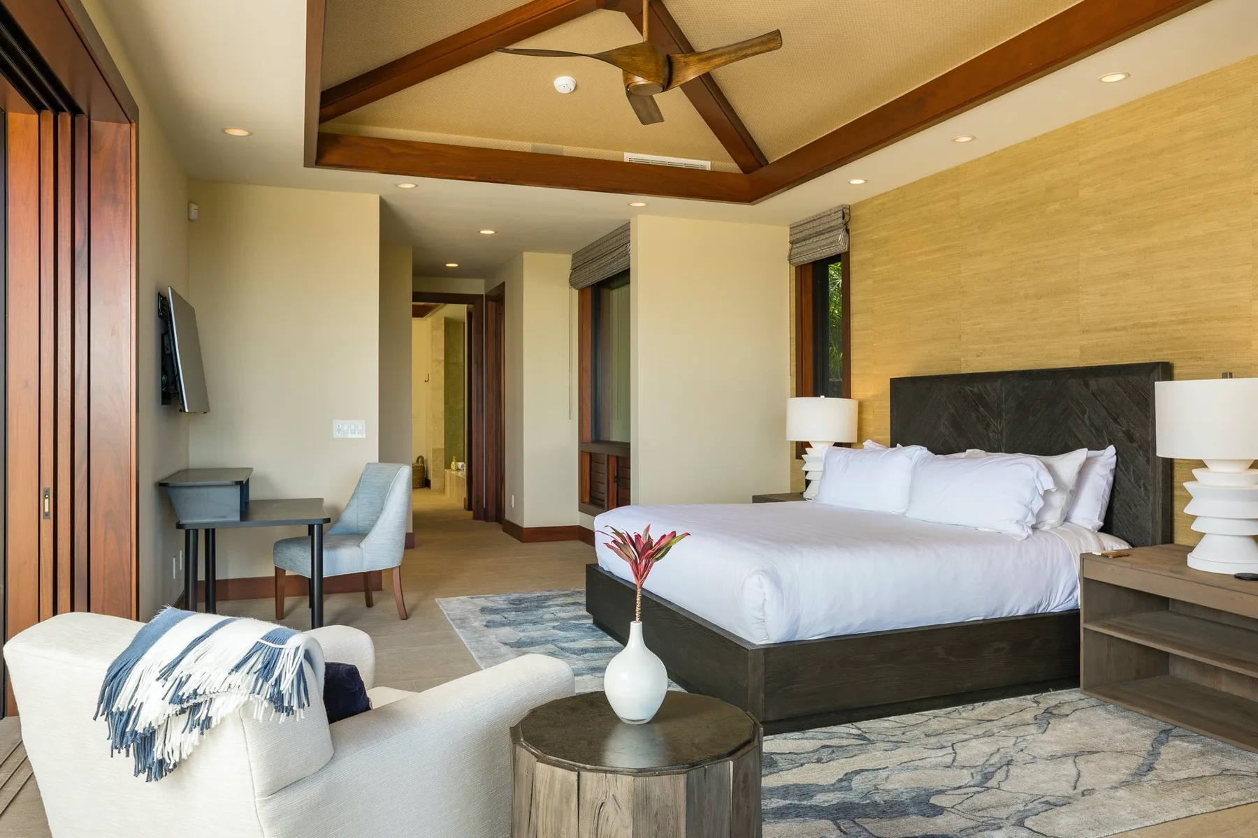 A bedroom with a large bed, a sitting area, and exposed ceiling beams.