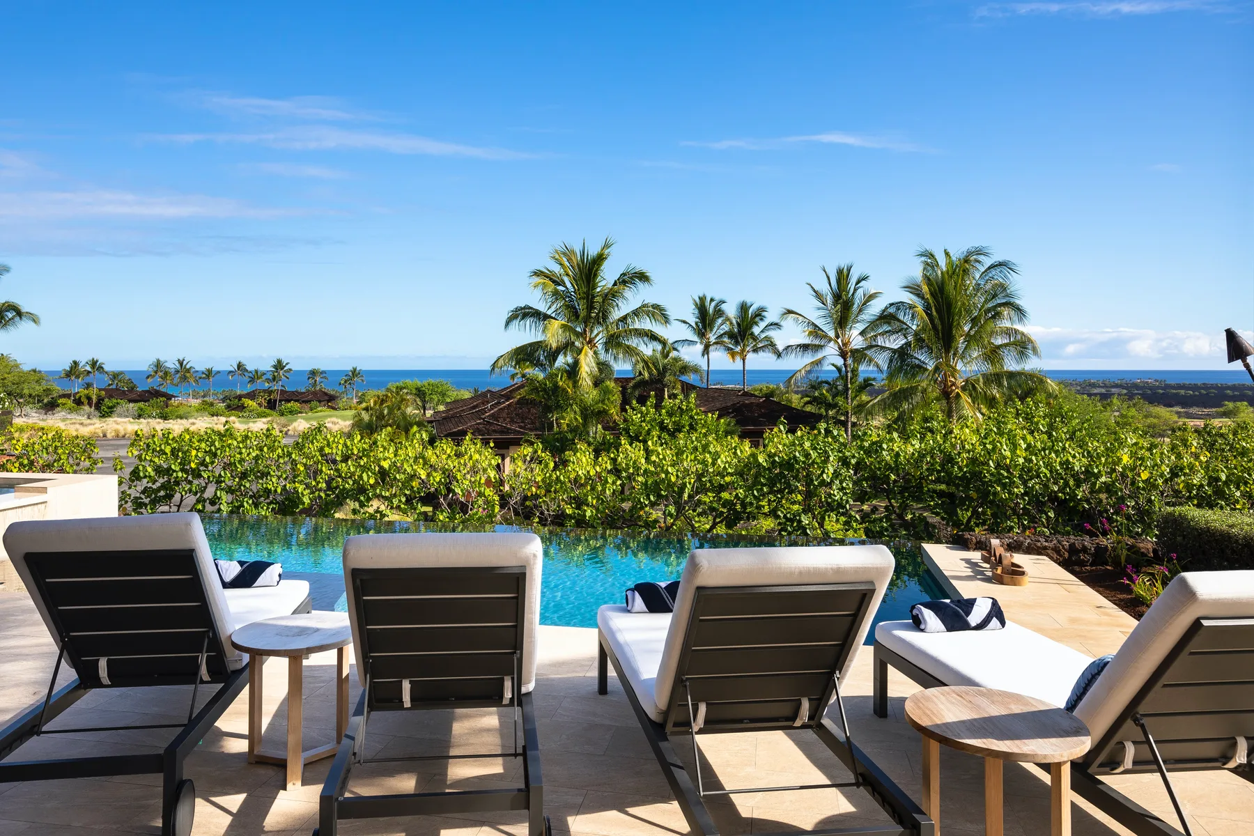 An outdoor poolside seating area overlooks palm trees and the ocean.