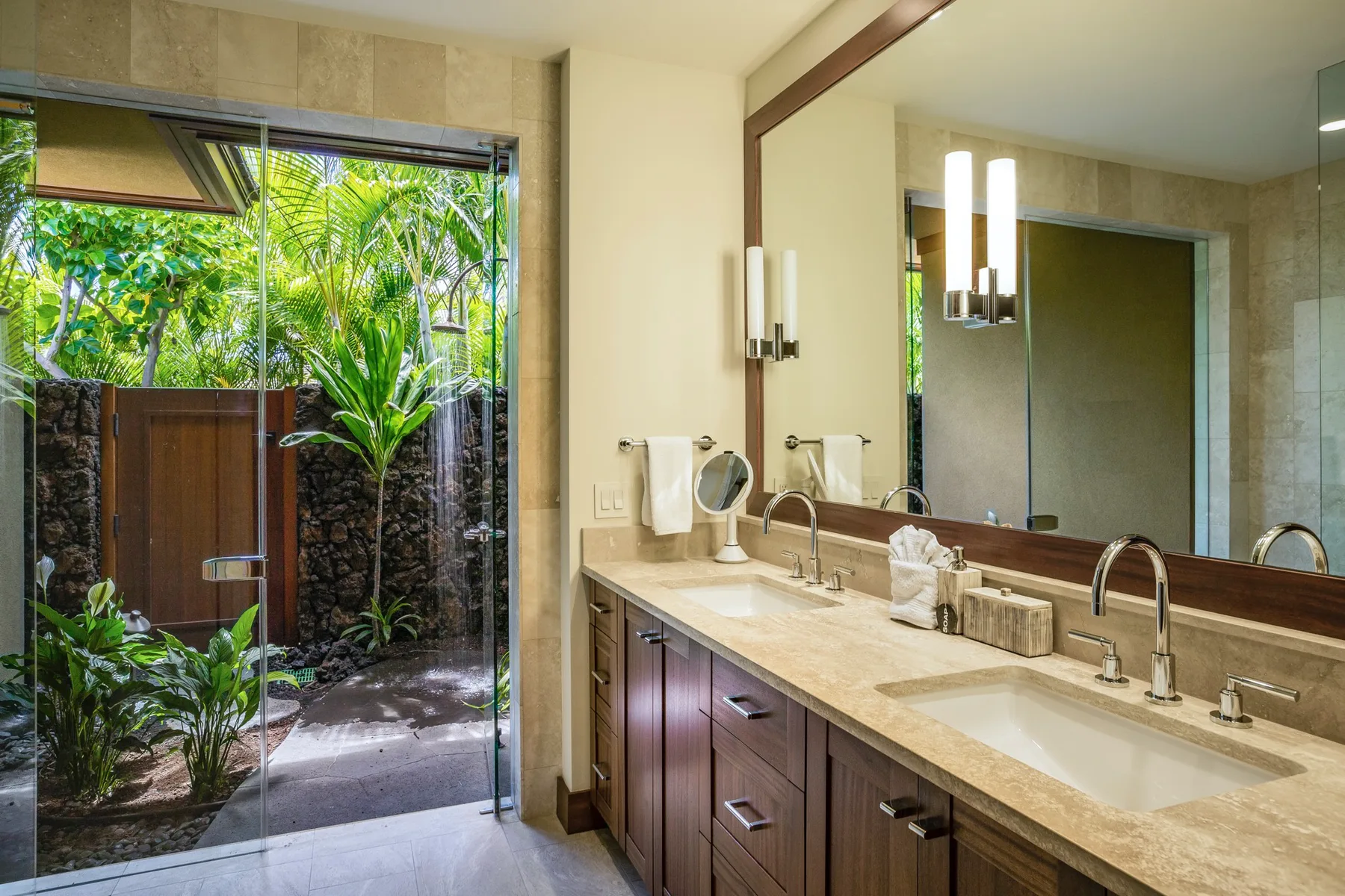 A bathroom vanity with twin sinks overlooks a lush outdoor garden.