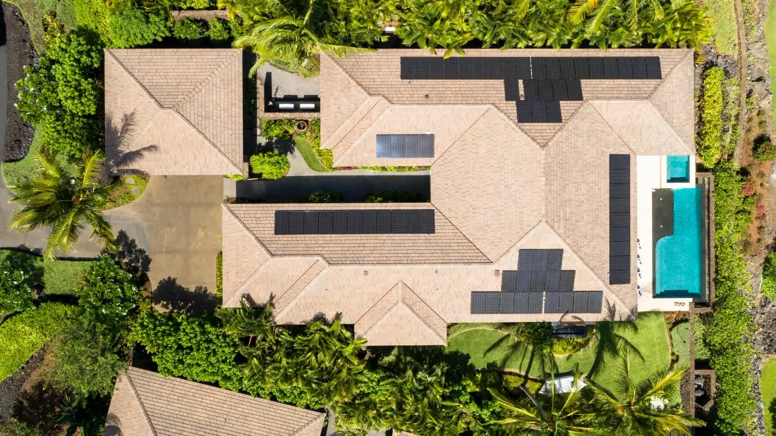 An aerial view of a tiled-roof building with solar panels and a swimming pool.