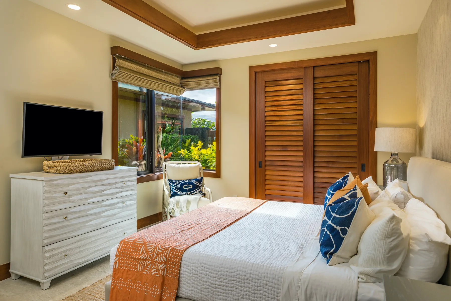 A bedroom with a bed, a dresser, and a window overlooking greenery.