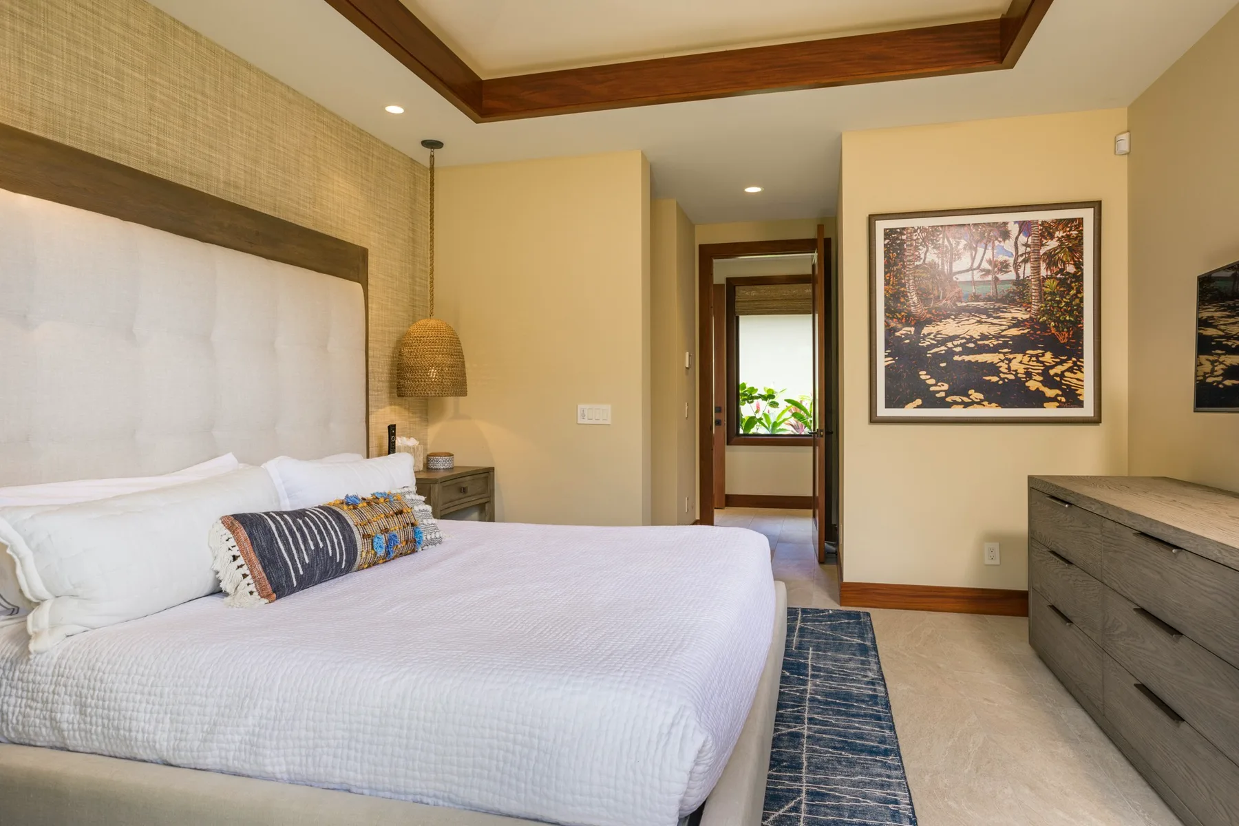 A bedroom with a large bed, framed artwork, and a dresser.