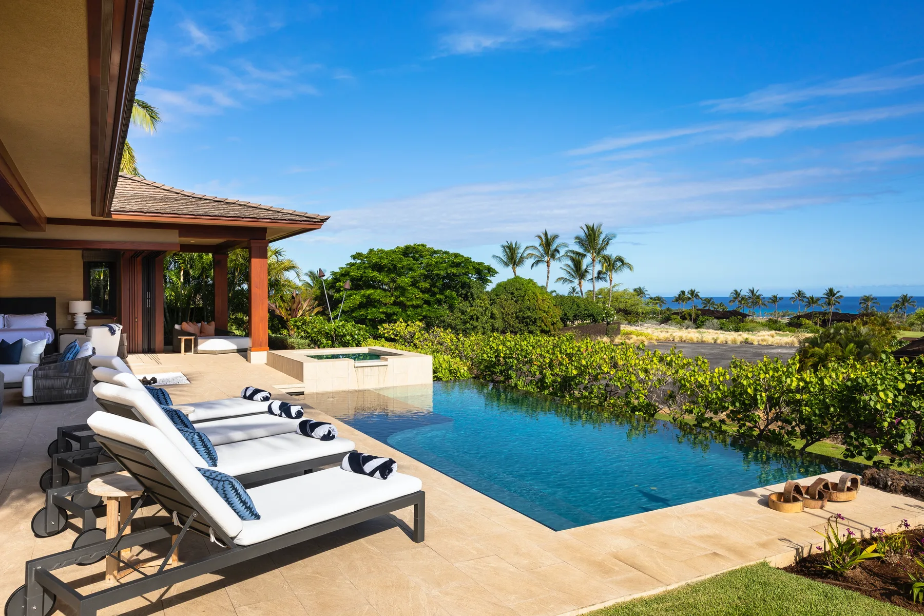 A poolside patio with lounge seating overlooks greenery and the ocean.