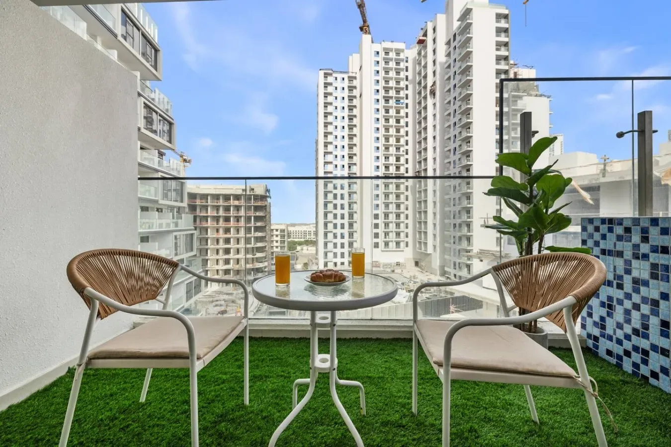Una zona de estar en el balcón con una mesa pequeña, una planta y edificios de la ciudad tras la barandilla de vidrio.