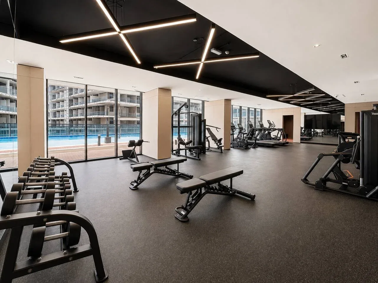 Un gimnasio amplio con máquinas de ejercicio y bancos junto a grandes ventanales.