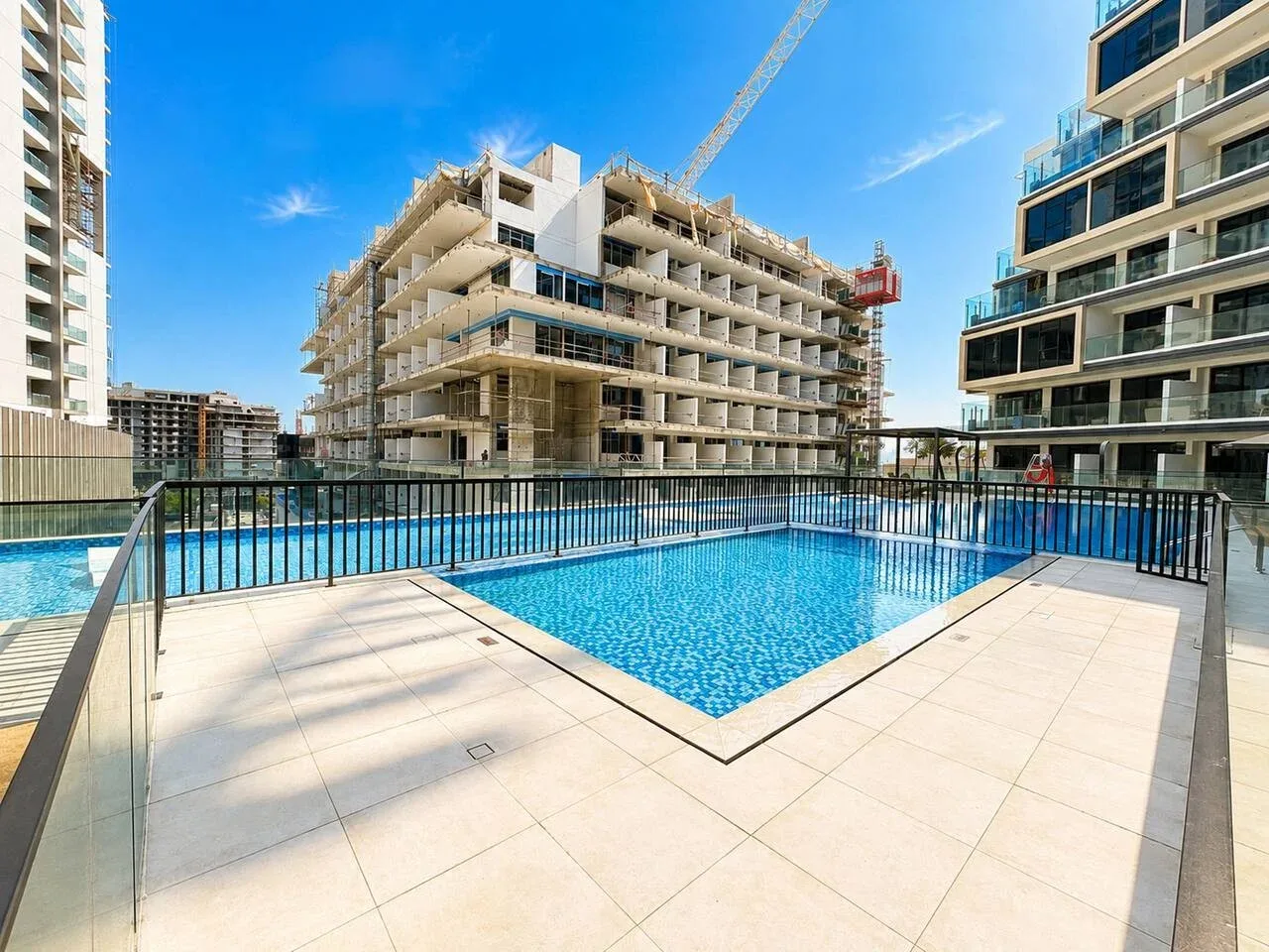 Una piscina al aire libre junto a edificios modernos, con una grúa de construcción al fondo.