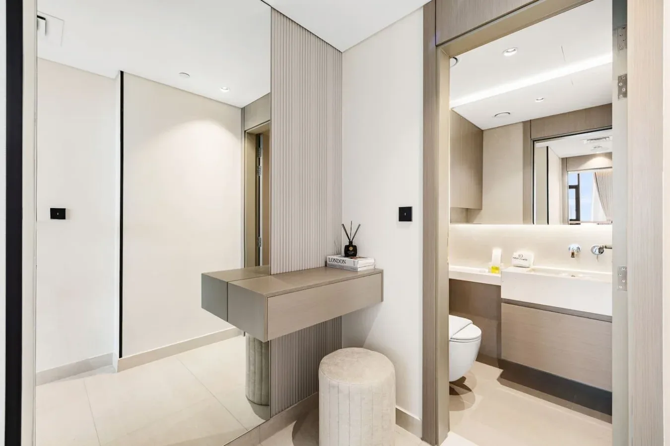 Una zona de tocador luminosa junto a un baño abierto con lavabo y espejo.