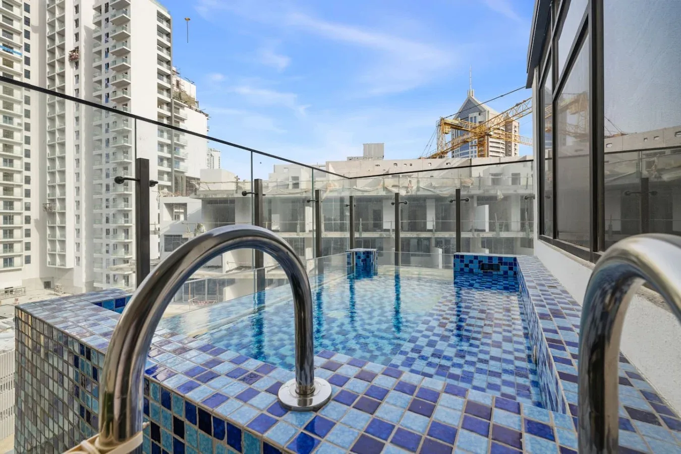 Una piscina en la azotea con mosaicos azules y edificios urbanos alrededor.