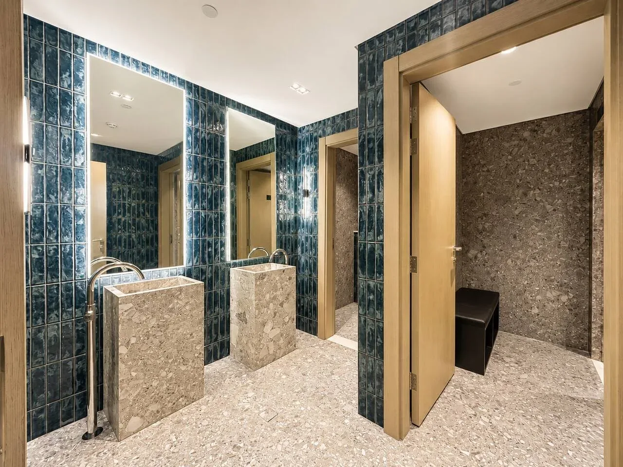 Un baño con azulejos, lavabos de piedra y una puerta con marco de madera.