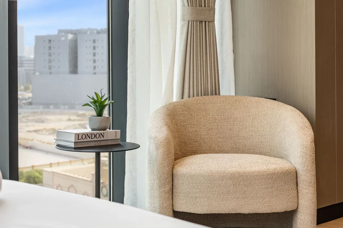Zona de estar de un dormitorio con un sillón beige junto a una ventana.