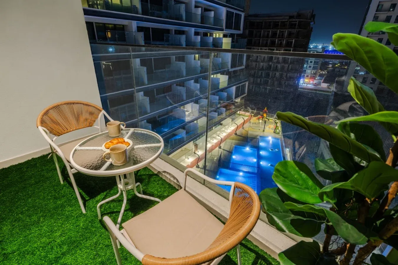 Una zona de estar en el balcón da a una piscina iluminada por la noche.