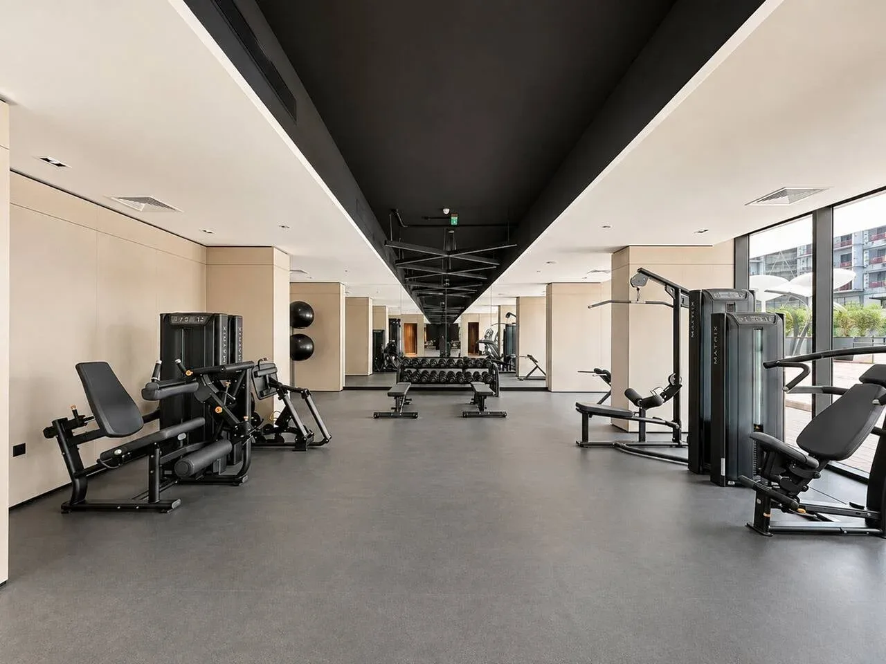 Un gimnasio con máquinas de ejercicio, pesas y grandes ventanales.