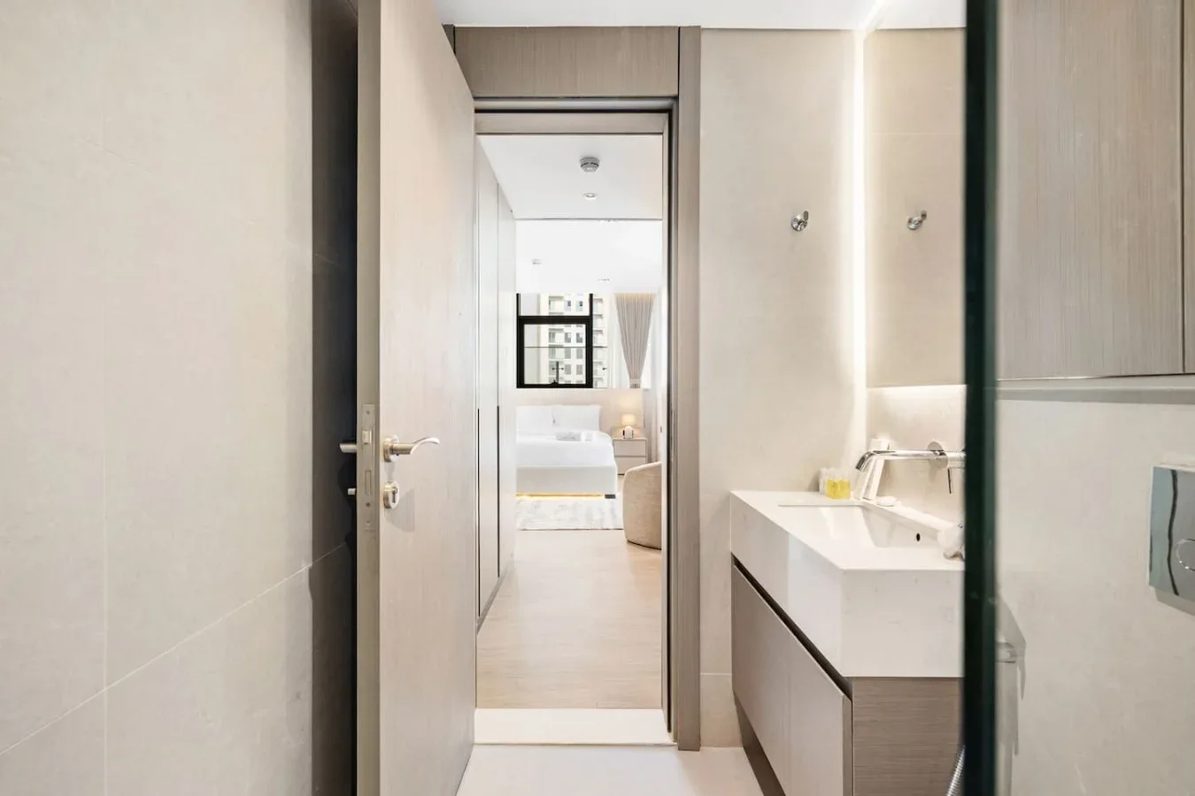 Un lavabo de baño está junto a una puerta abierta que da a un dormitorio.