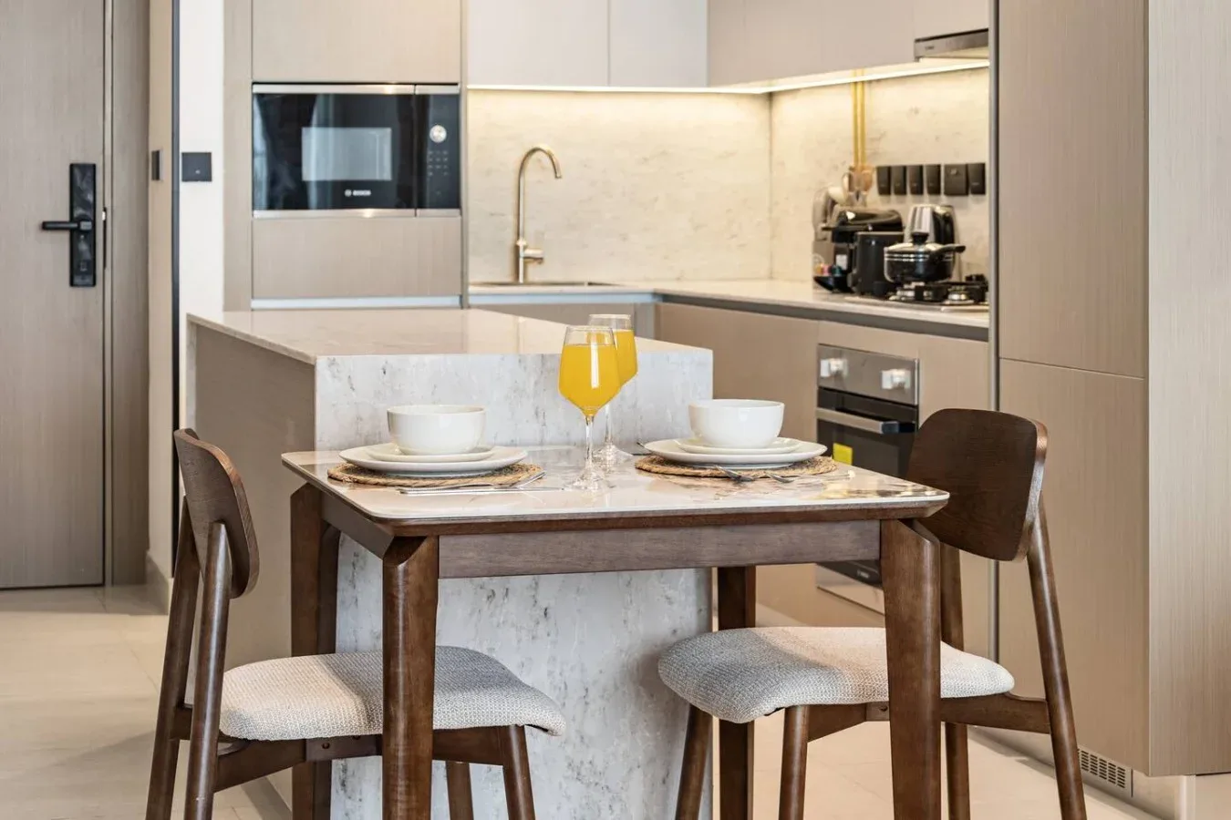 Una mesa de comedor con cubiertos y una bebida está junto a una cocina moderna.