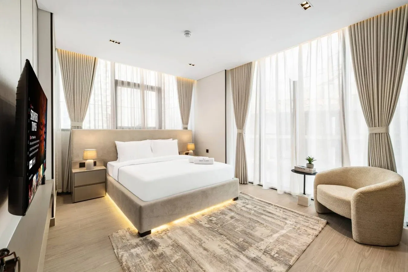 Un dormitorio luminoso con una cama grande, cortinas largas y un sillón.