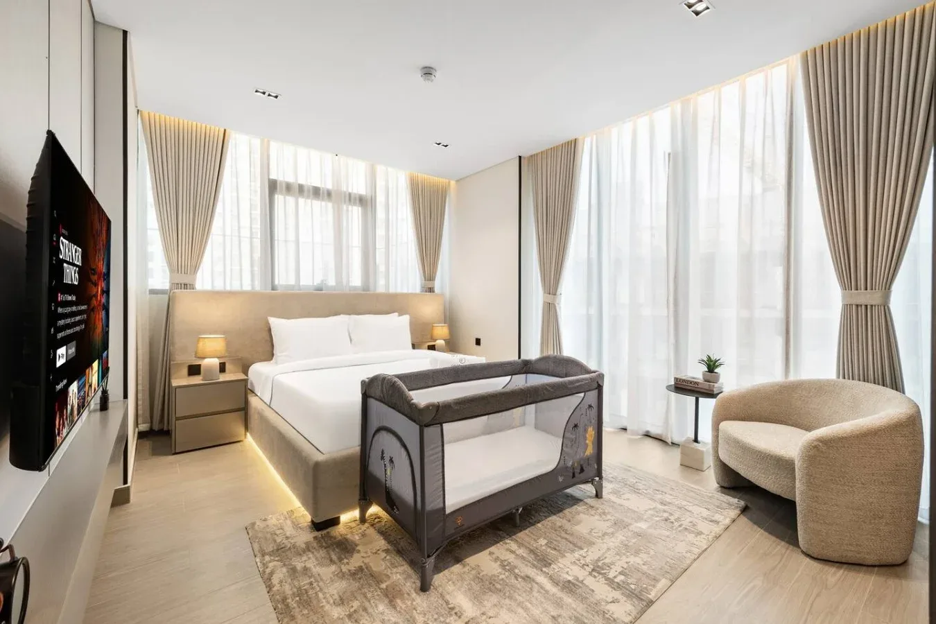 Un dormitorio luminoso con una cama grande, una cuna y cortinas de techo a suelo.