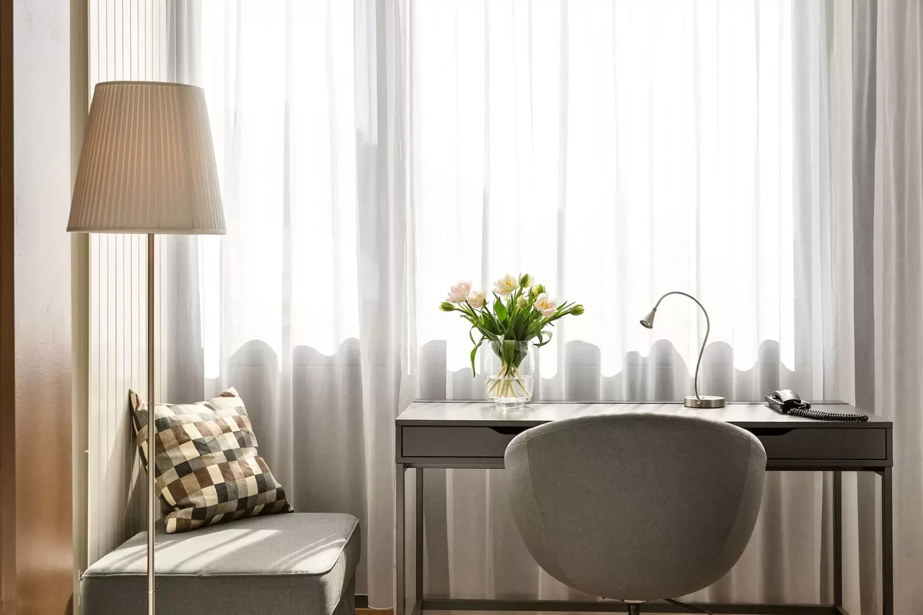 Desk and chair by a window with flowers and a table lamp.