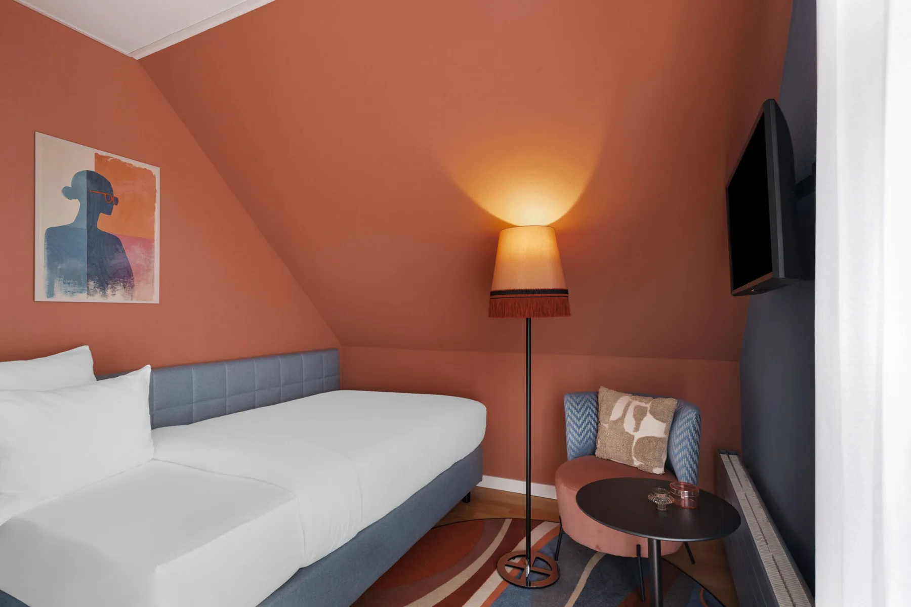 Basic single room with a single bed, armchair, side table, floor lamp and television.