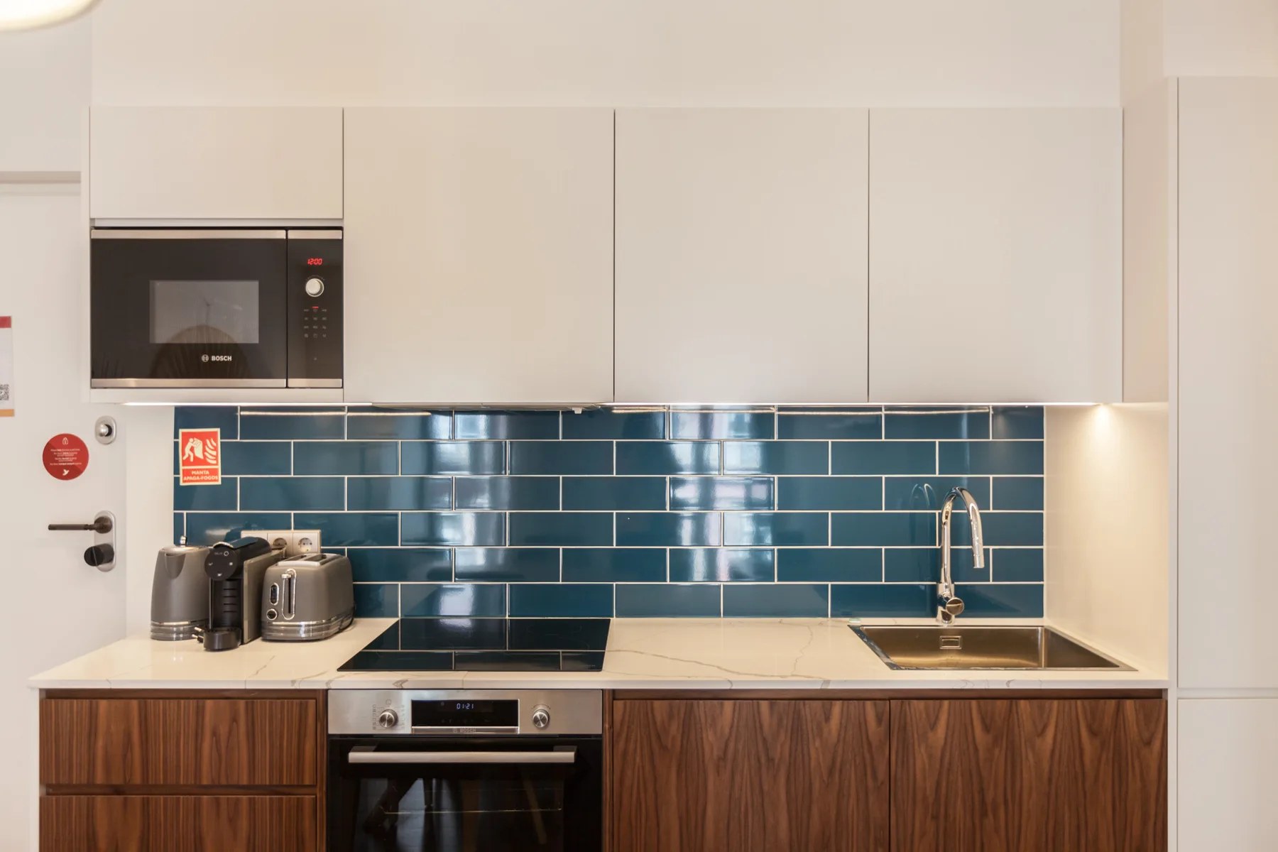 A modern kitchen with blue backsplash tiles and light cabinetry.