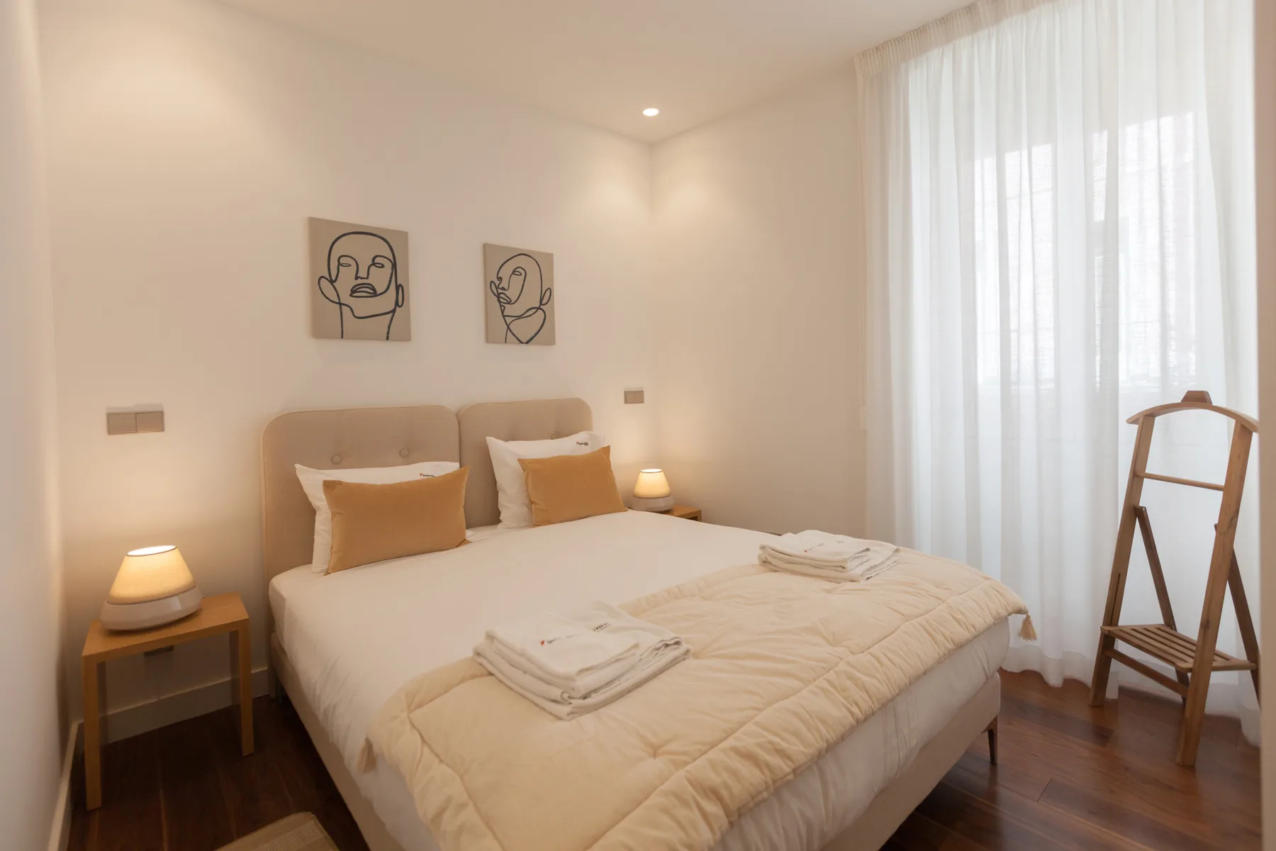 A bright bedroom with a neatly made bed and sheer curtains.