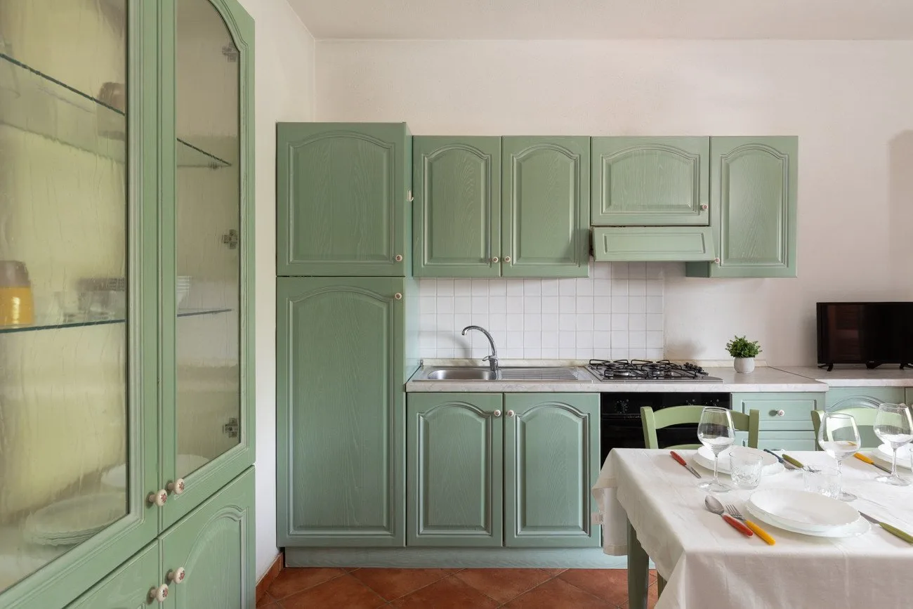 Una cocina con armarios verdes, un salpicadero de azulejos y una mesa de comedor.
