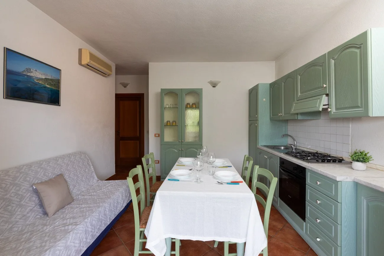 Comedor con una mesa puesta junto a un sofá y armarios de cocina verdes.