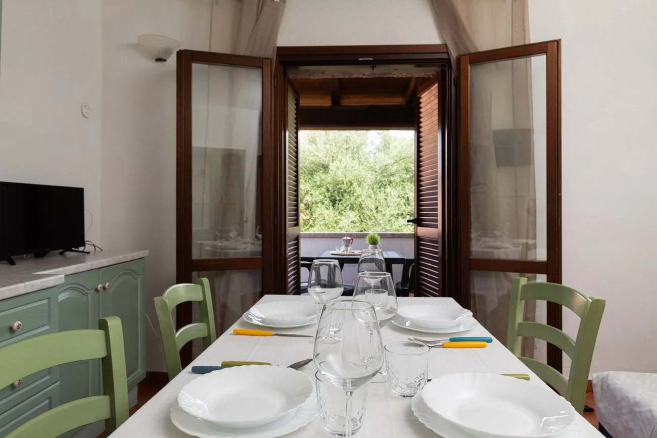 Una mesa está puesta con platos y vasos junto a puertas abiertas con vistas a la vegetación.