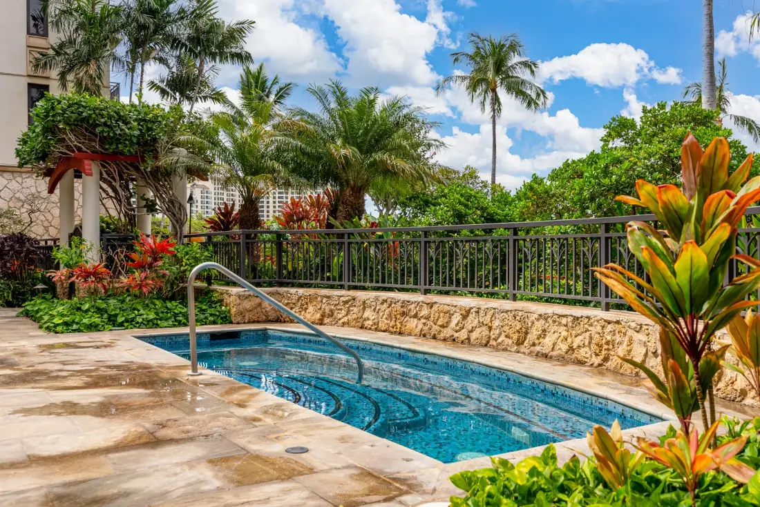 Una pequeña piscina al aire libre está rodeada de vegetación tropical y pavimento de piedra.
