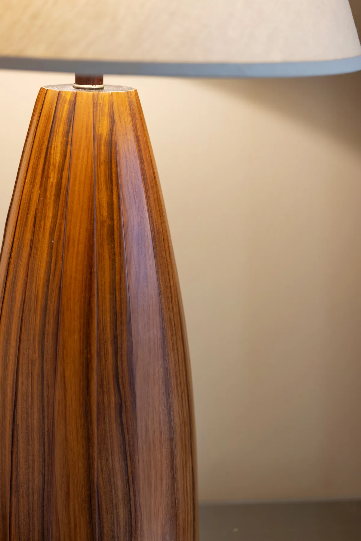 Una lámpara de mesa con base de madera está frente a una pared lisa.