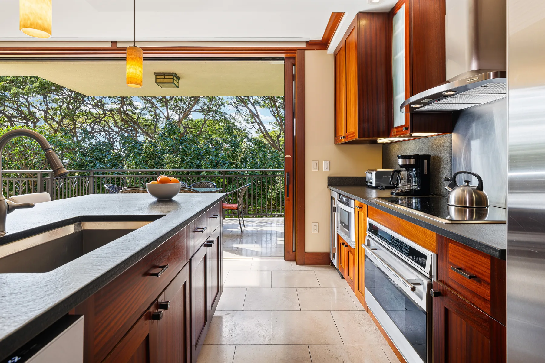 Una cocina luminosa con una isla central y árboles frondosos visibles por las puertas abiertas.