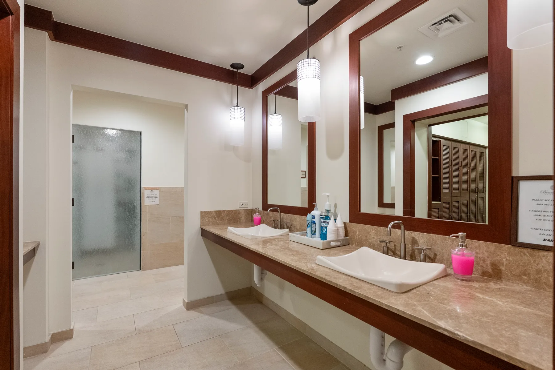 Un lavabo de baño con espejos y lavamanos, con una ducha al fondo.