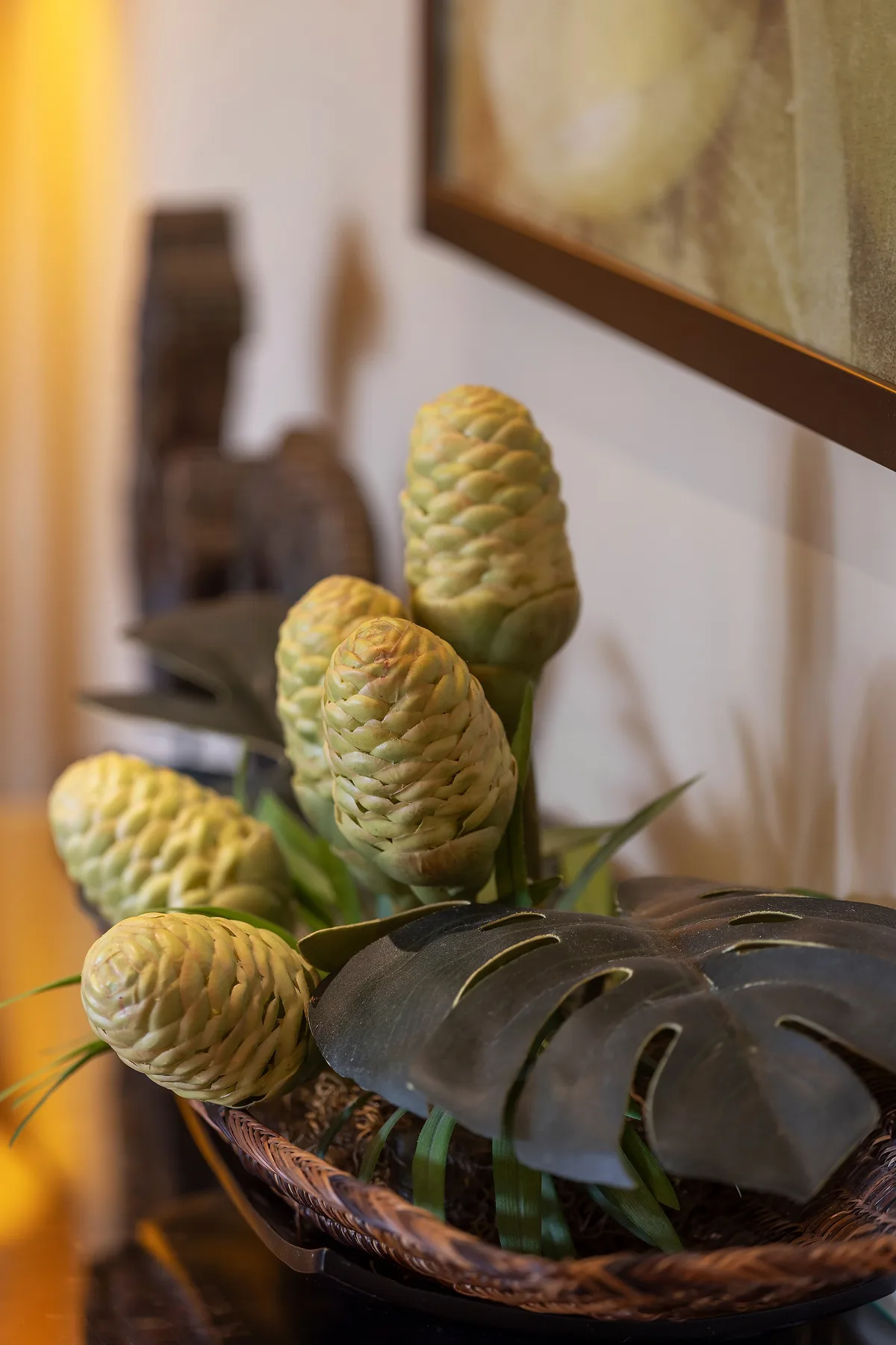Un arreglo decorativo de hojas verdes y vainas claras con textura está en un cuenco bajo.