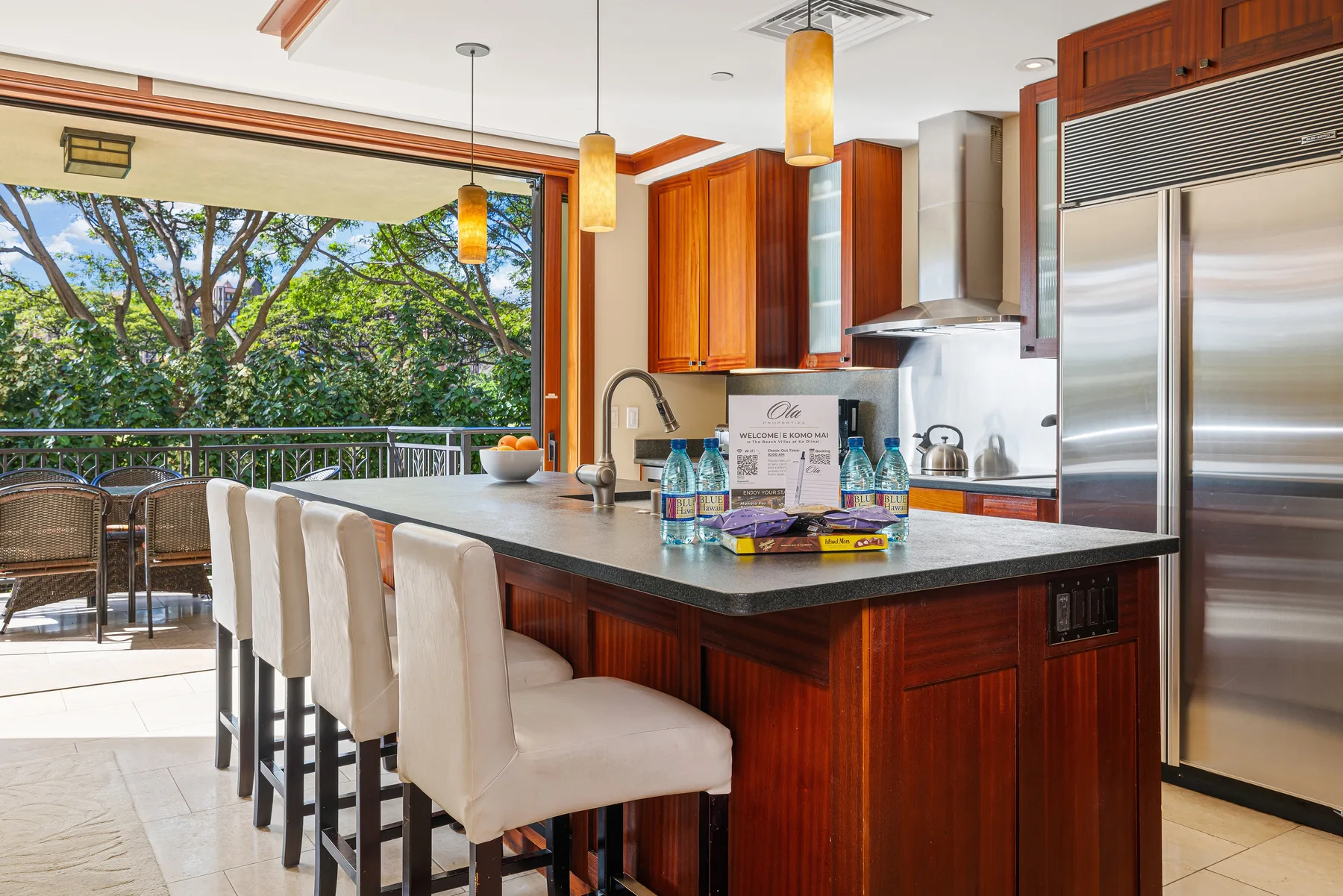 Una cocina con una isla grande y asientos junto a un patio abierto.