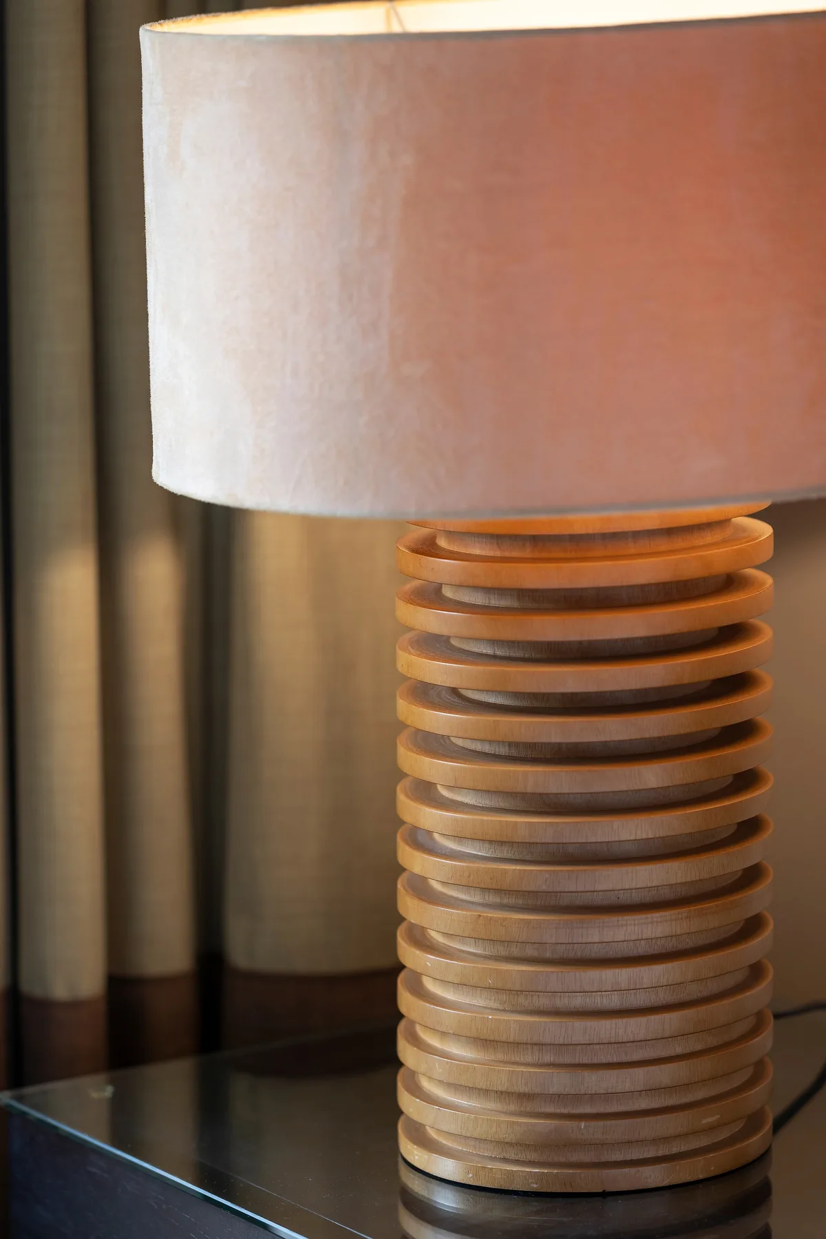 Una lámpara de mesa con base acanalada está frente a unas cortinas.