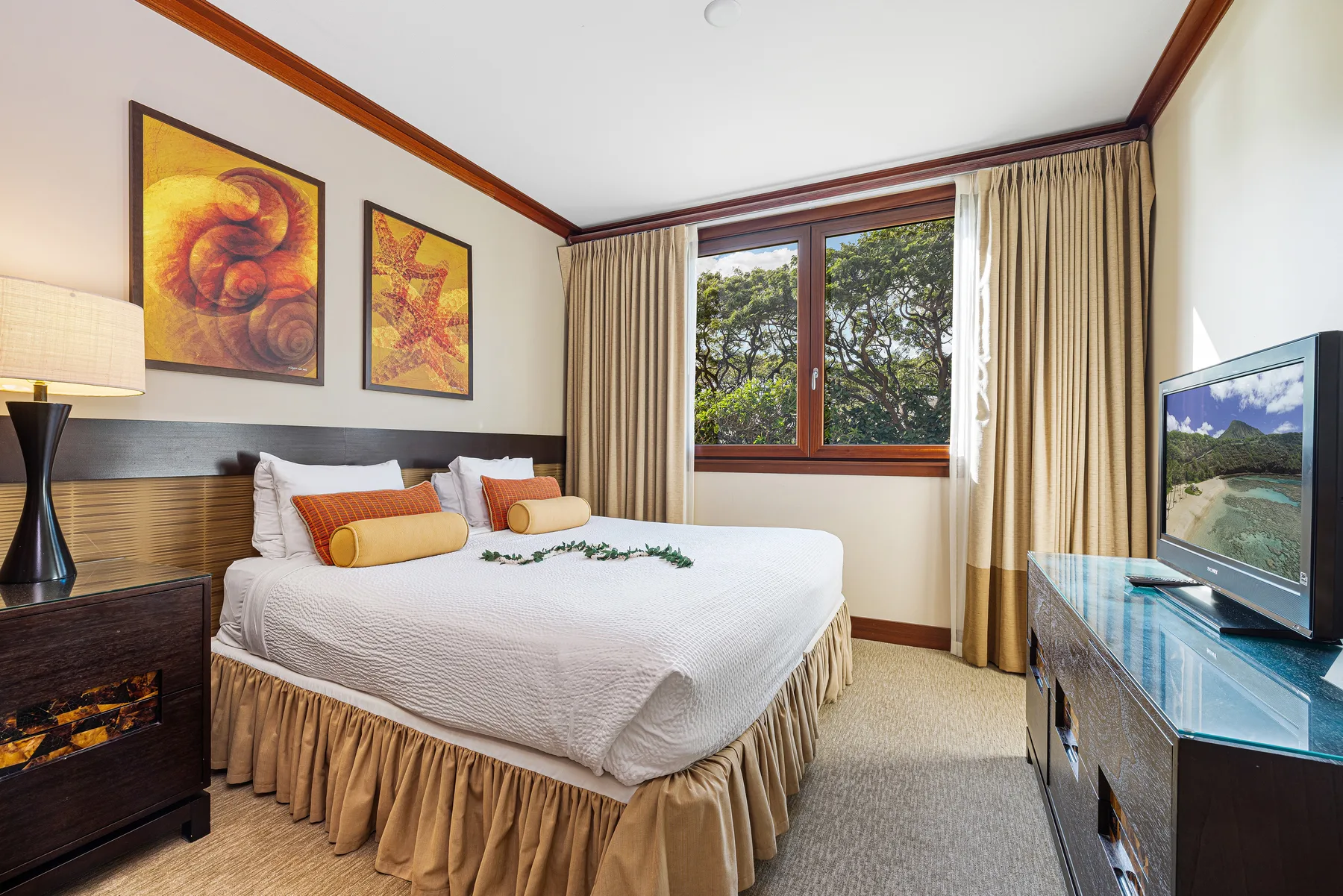 Un dormitorio con una cama bien tendida, cuadros enmarcados y una ventana con vista a los árboles.