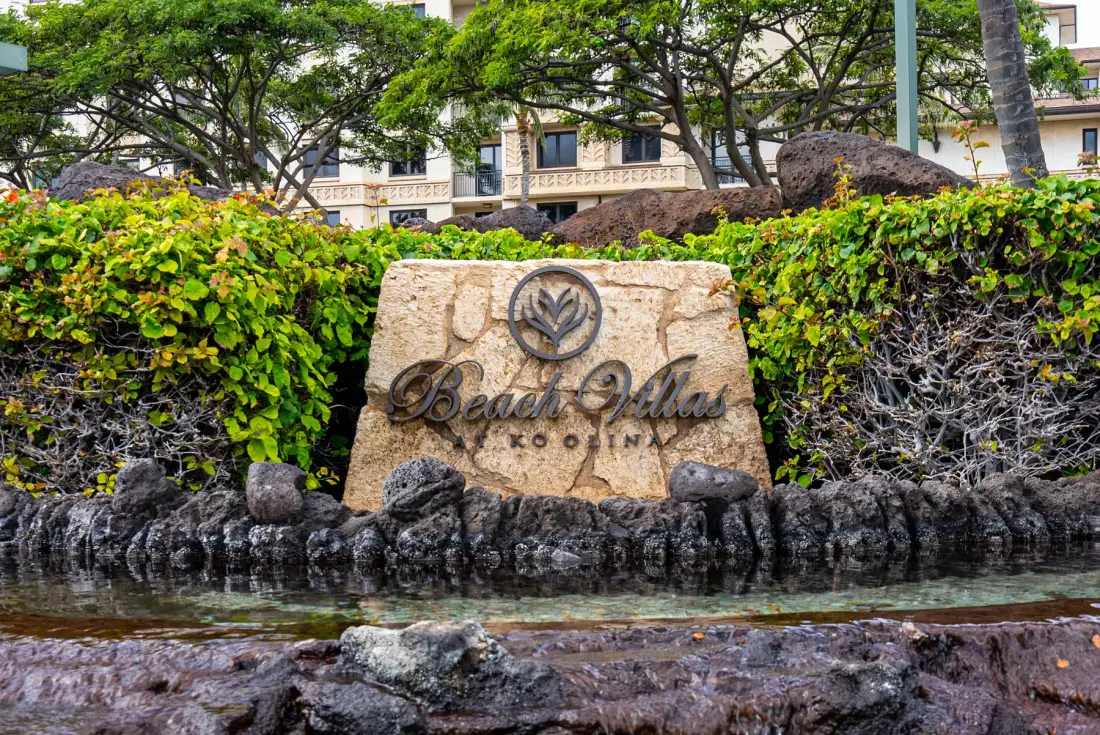 La entrada ajardinada de un hotel muestra un letrero de piedra entre setos y rocas.
